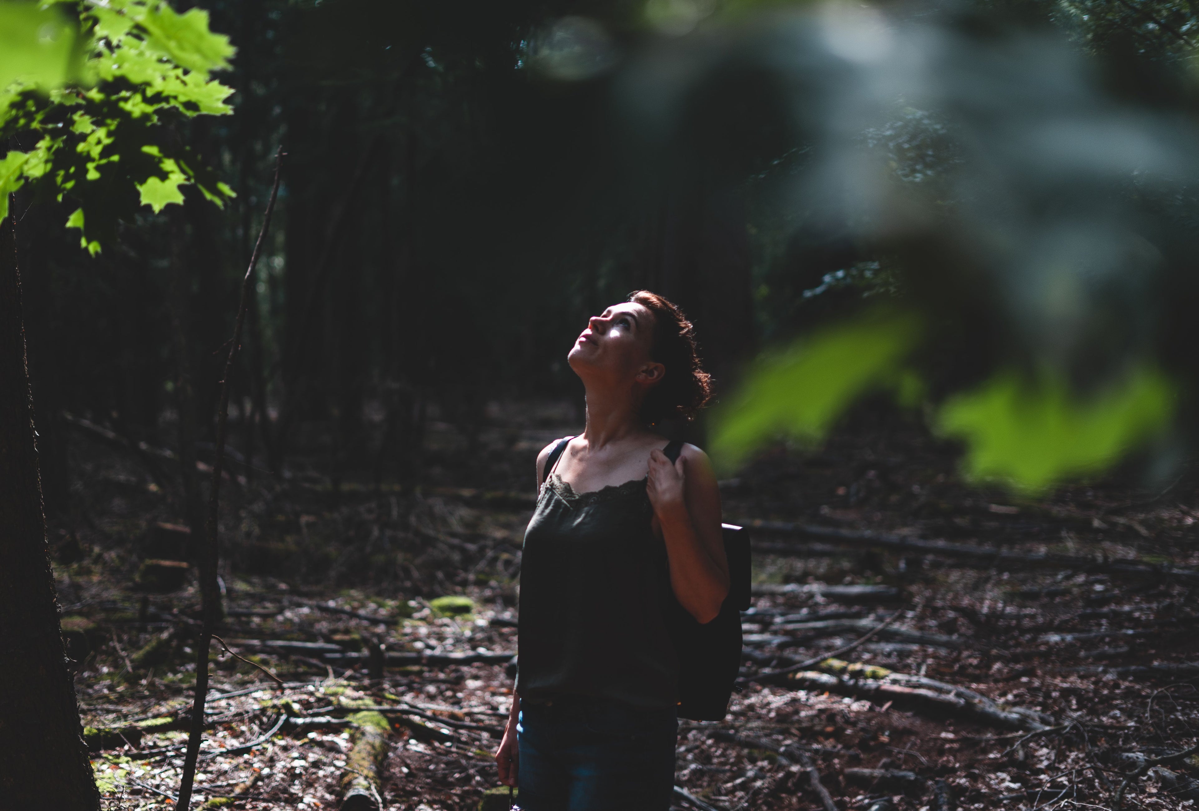 femme qui lève les yeux, feuillage vert en premier plan, forêt sombre